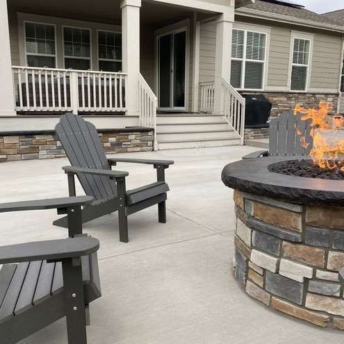 A fire pit with two chairs in front of a house.