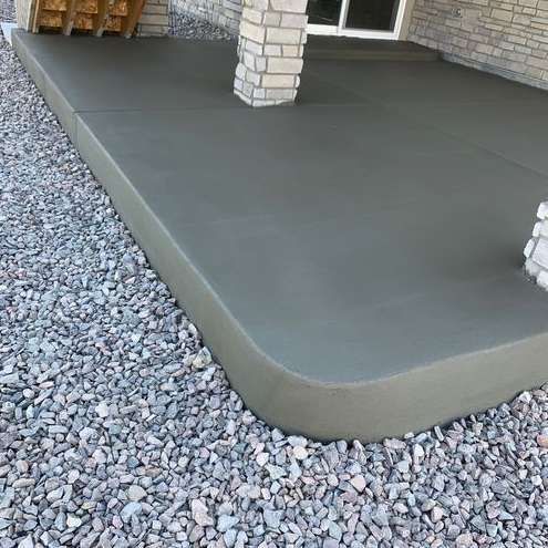 A concrete patio with a brick pillar in the background is surrounded by gravel.