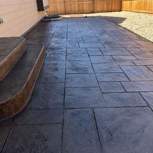 A concrete walkway with stairs and a wooden fence in the background.