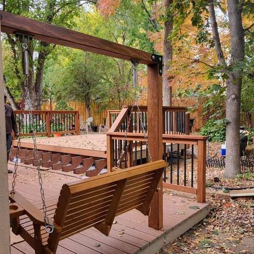 A wooden porch swing is sitting on top of a wooden deck.