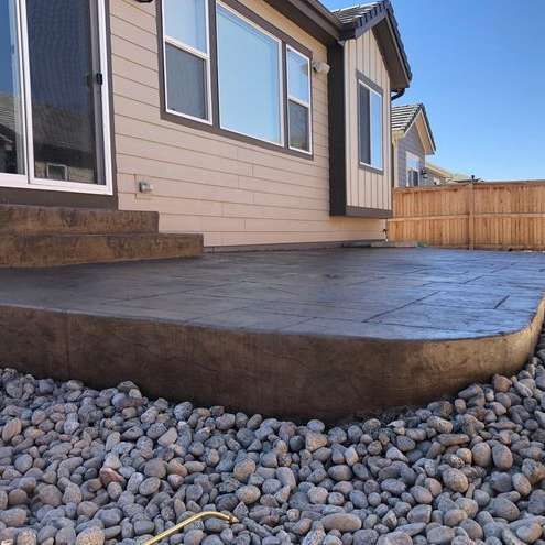 A concrete patio in front of a house surrounded by rocks.