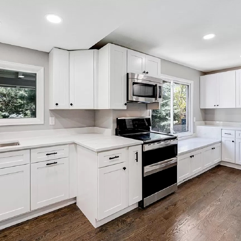 A kitchen with white cabinets , a stove , a microwave , and a window.
