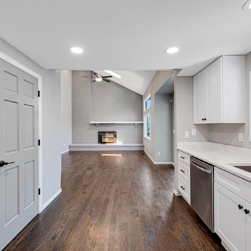 A kitchen with hardwood floors , white cabinets , stainless steel appliances and a fireplace.
