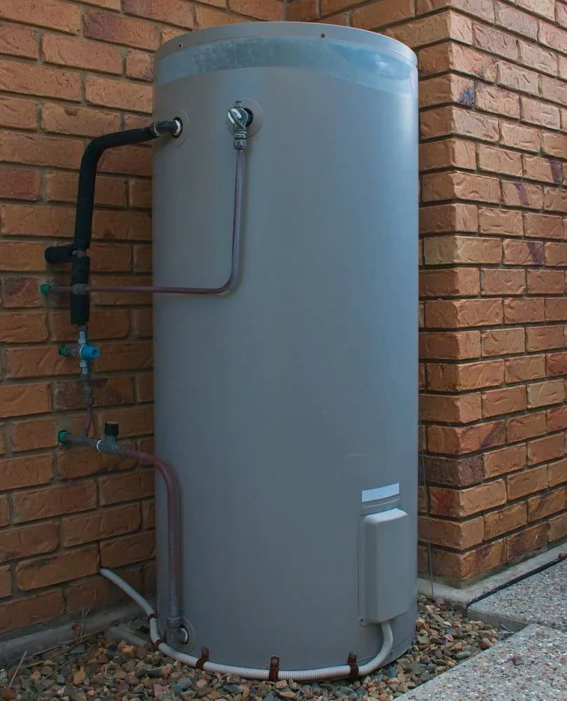 Gray Cylindrical Water Heater Beside a Brick Wall — The Plumbing & Drainage Co. in Moss Vale, NSW