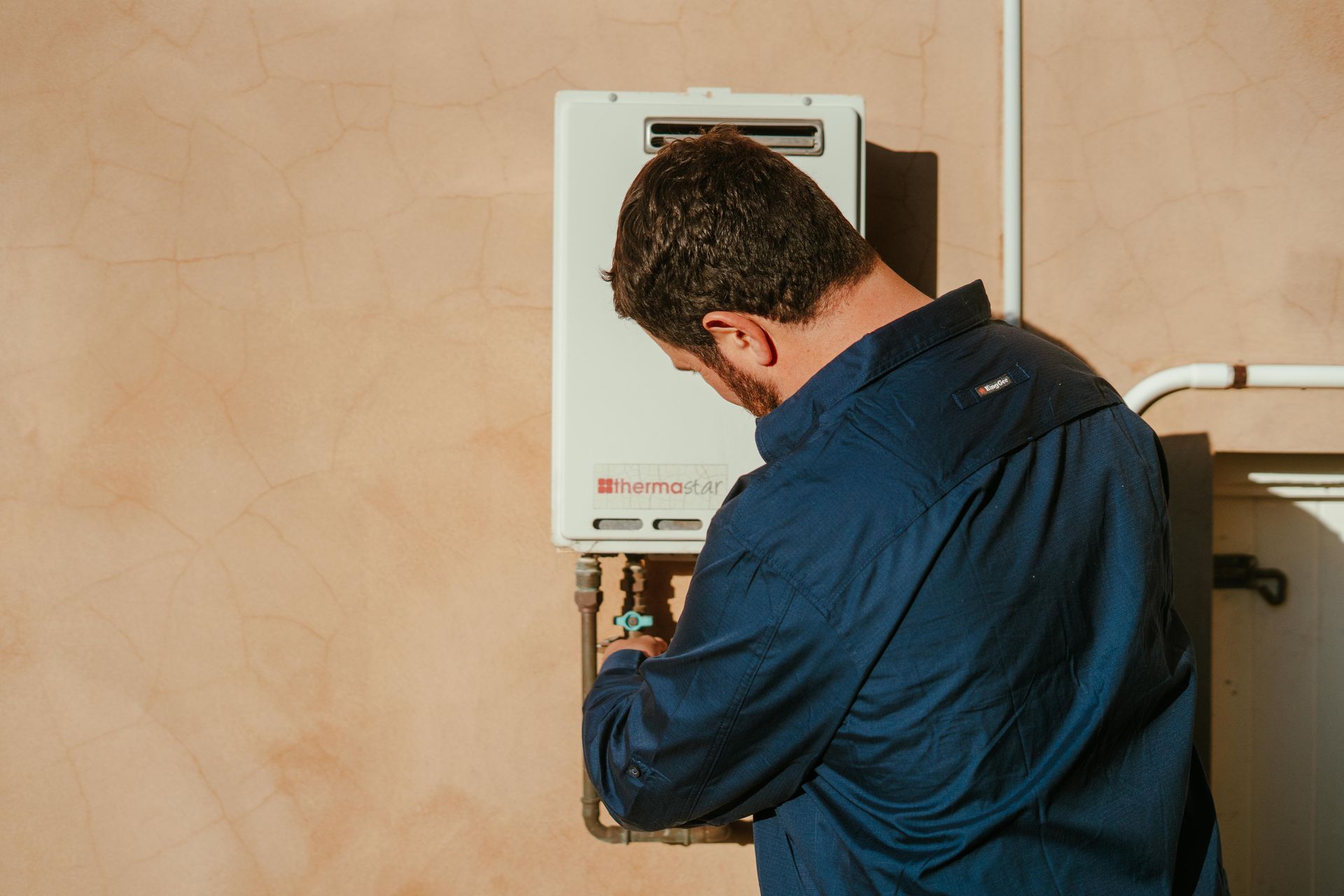 Technician repairing a wall-mounted boiler against a beige wall — The Plumbing & Drainage Co. in Moss Vale, NSW