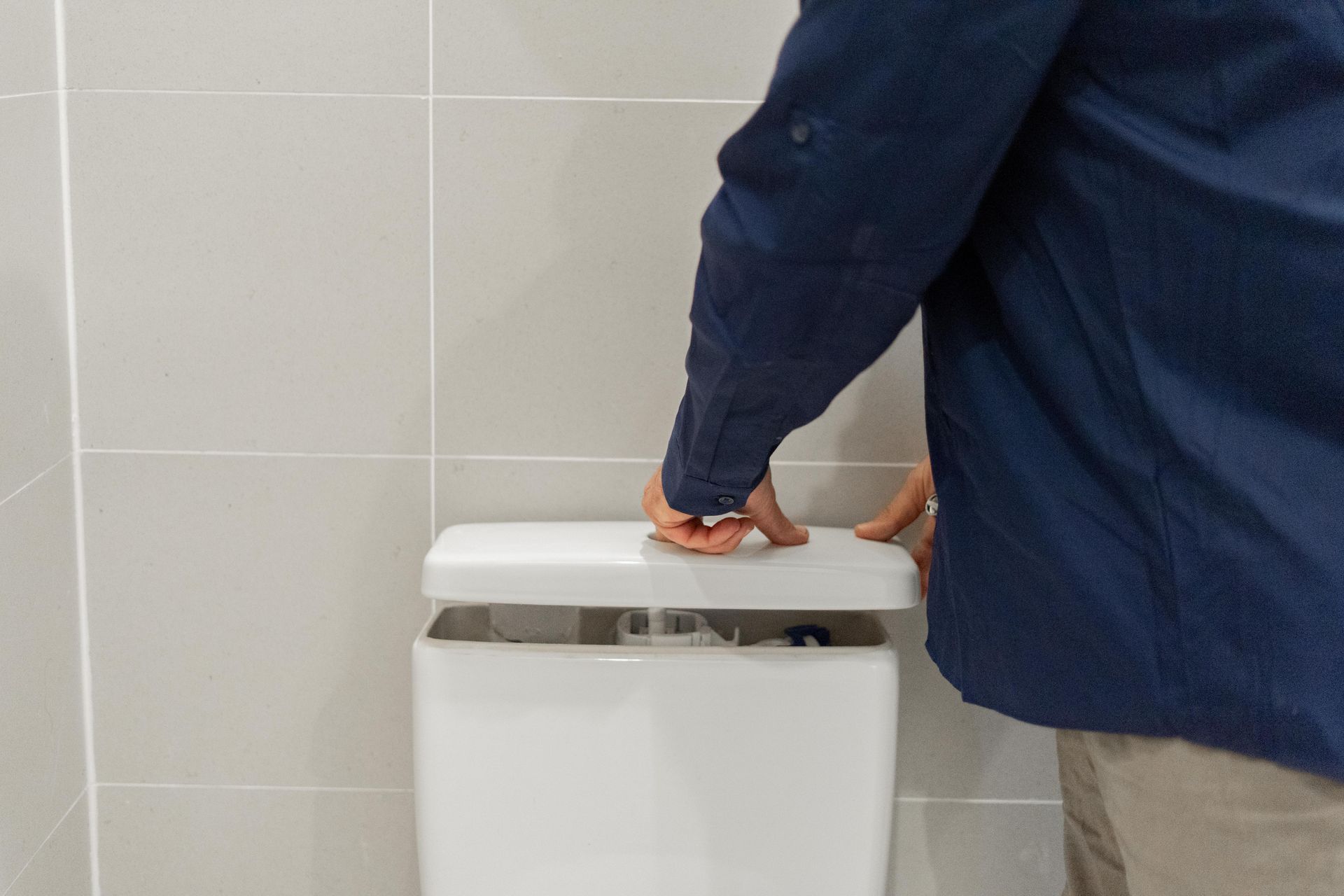Person in a blue shirt pressing on a white trash can lid in a tiled bathroom. — The Plumbing & Drainage Co. in Southern Highlands, NSW