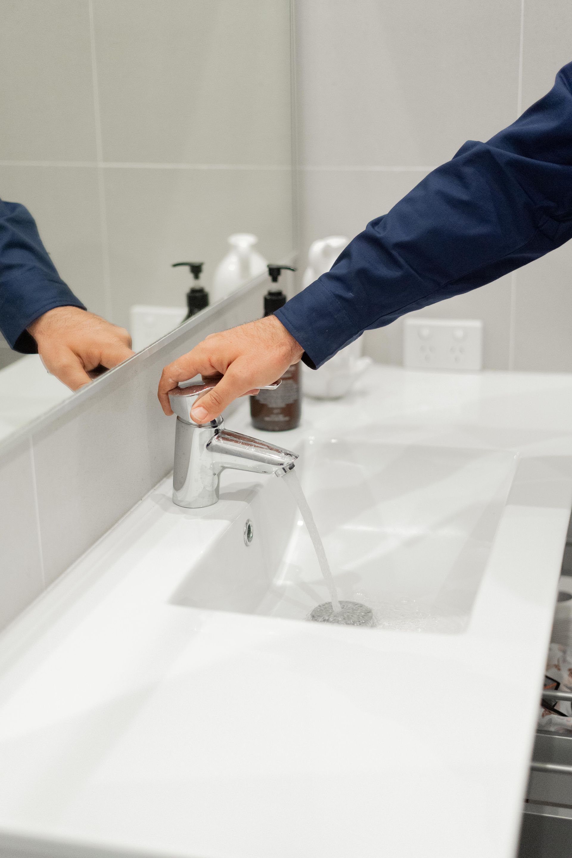 Hands washing at a white sink with running water in a tiled restroom — The Plumbing & Drainage Co. in Campbelltown, NSW