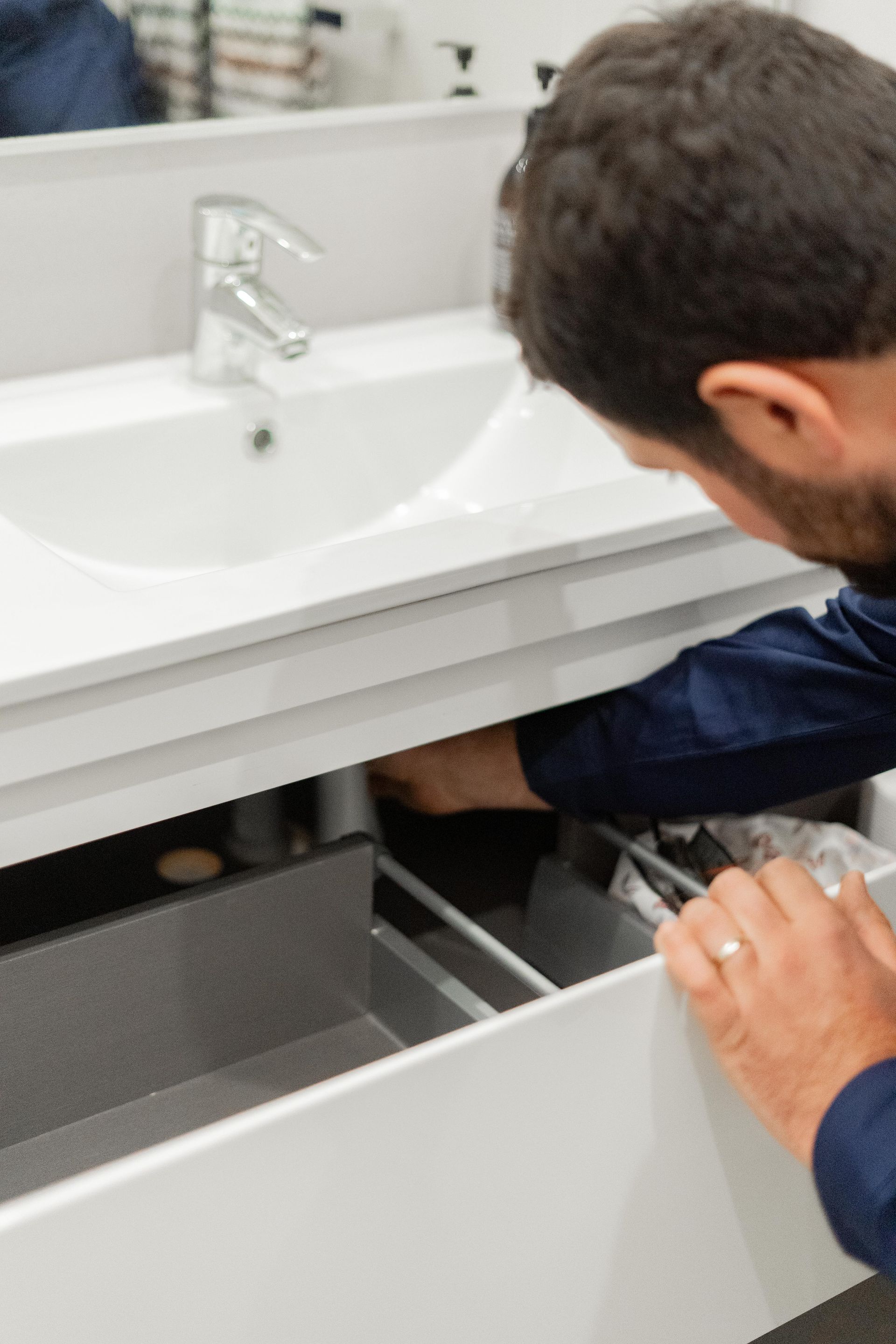 Person looking under an open white bathroom vanity cabinet with sink above. — The Plumbing & Drainage Co. in Mittagong, NSW