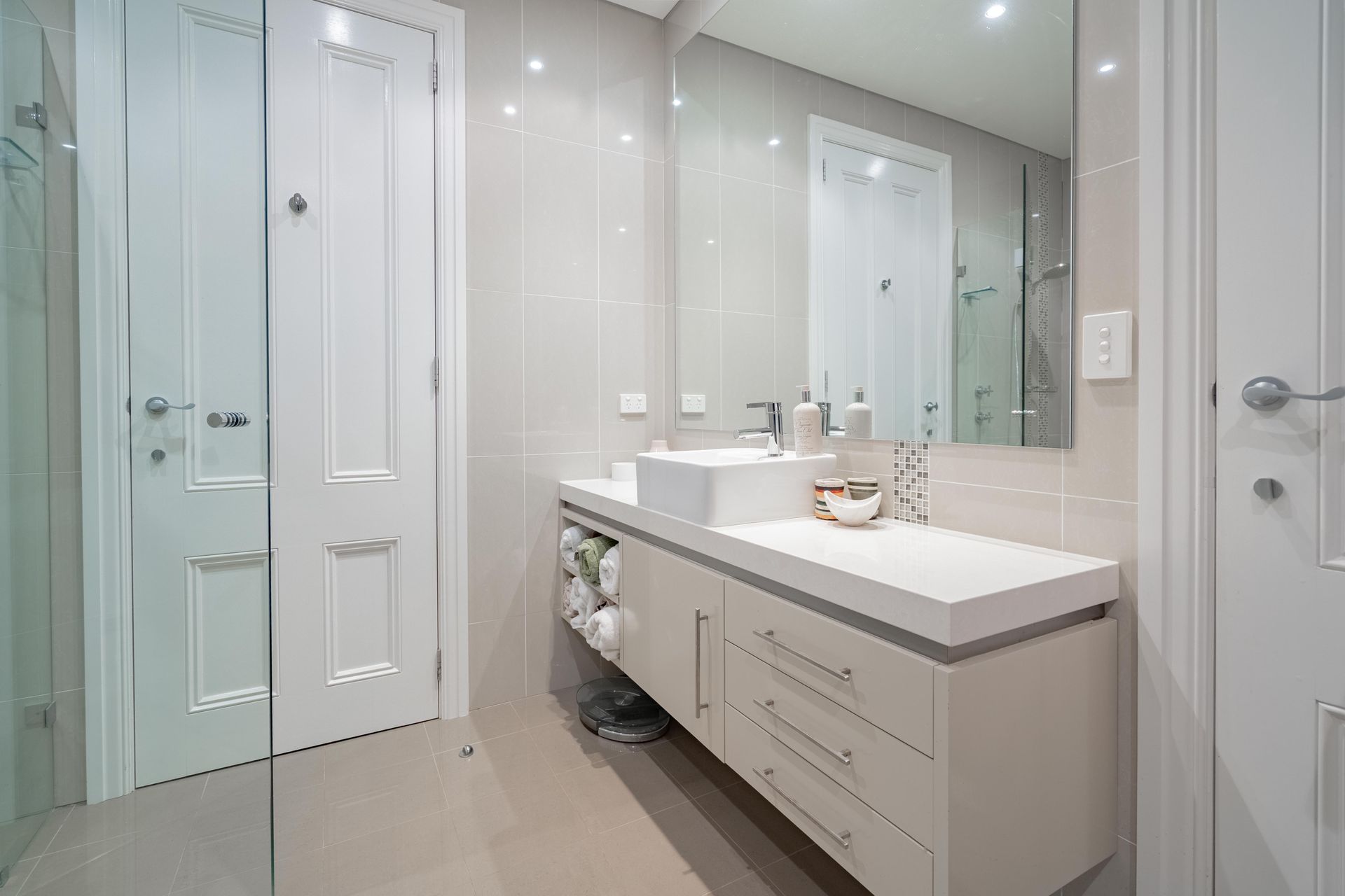 Modern white bathroom with double vanity, large mirror, glass shower, and tiled floor. — The Plumbing & Drainage Co. in Mittagong, NSW
