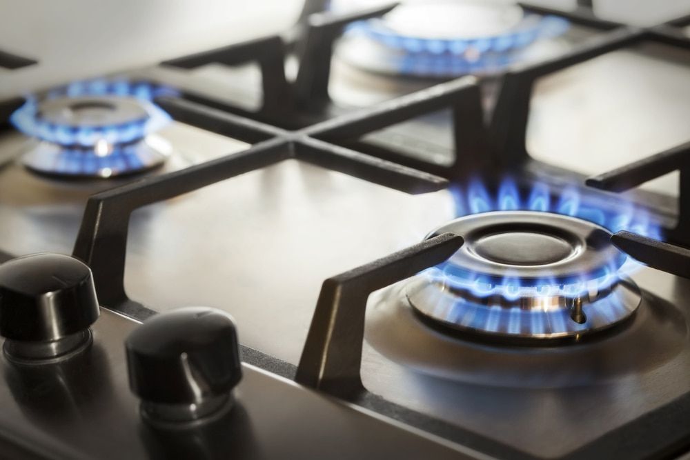 A Gas Stove With Blue Flames on Black Burners and Silver Grates — The Plumbing & Drainage Co. in Mittagong, NSW