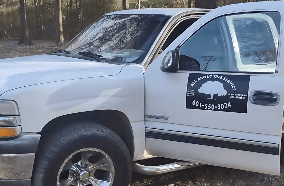 A white truck with a tree on the side is parked in the woods.
