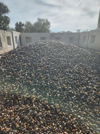 A pile of gravel is sitting in front of a fence