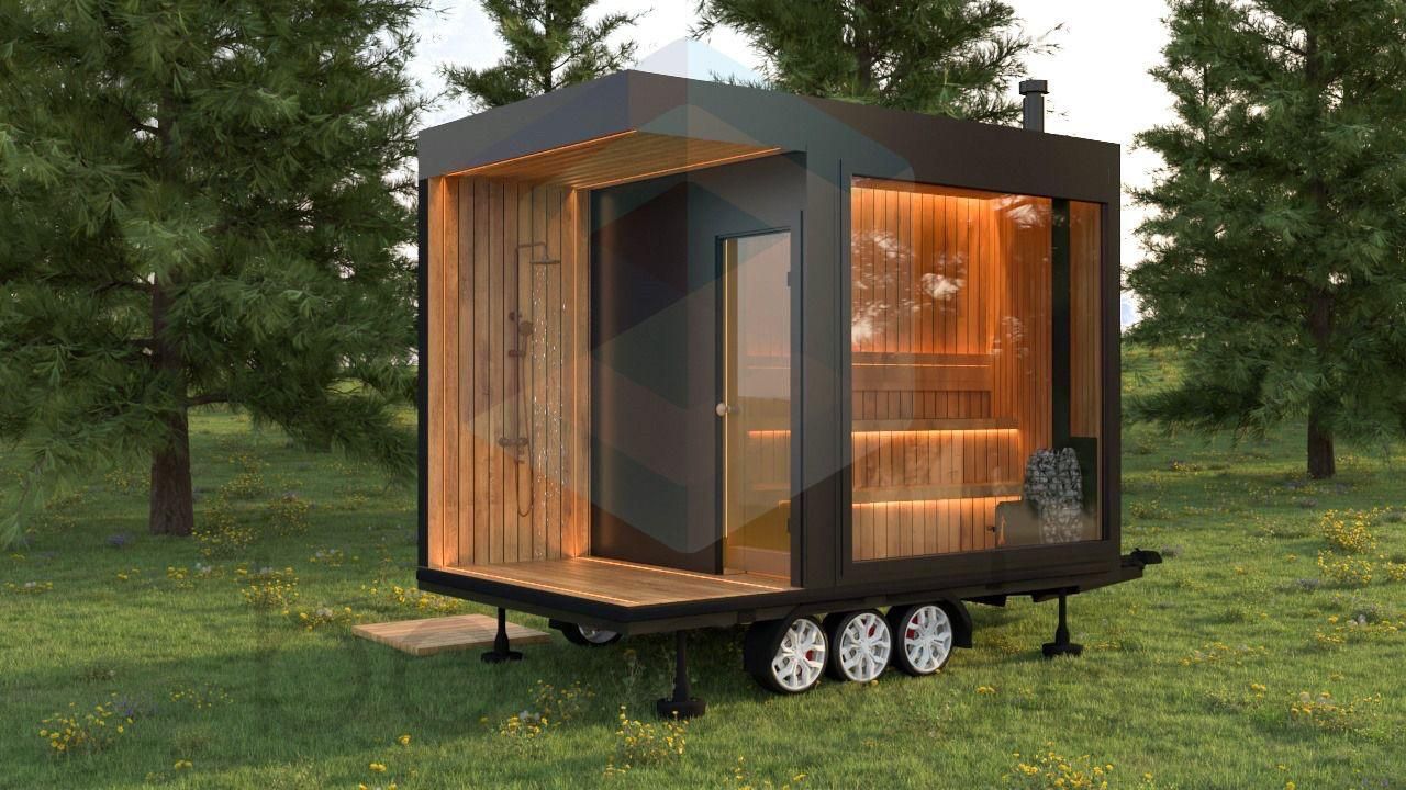 A mobile sauna with wood interior and glass wall on a trailer, set in a grassy area with trees.