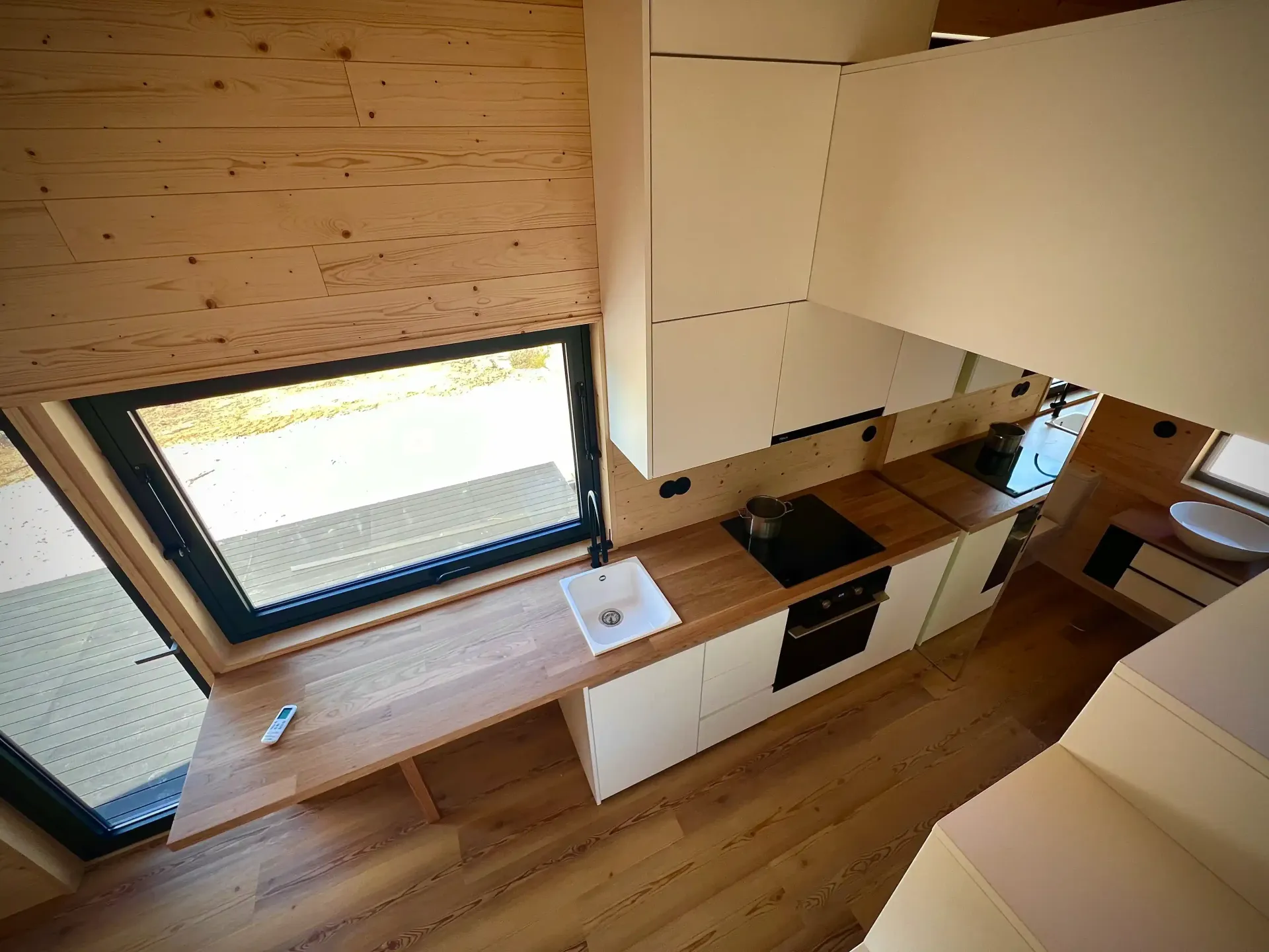 Interior view of a tiny home kitchen with wood counters, white cabinets, and a window.