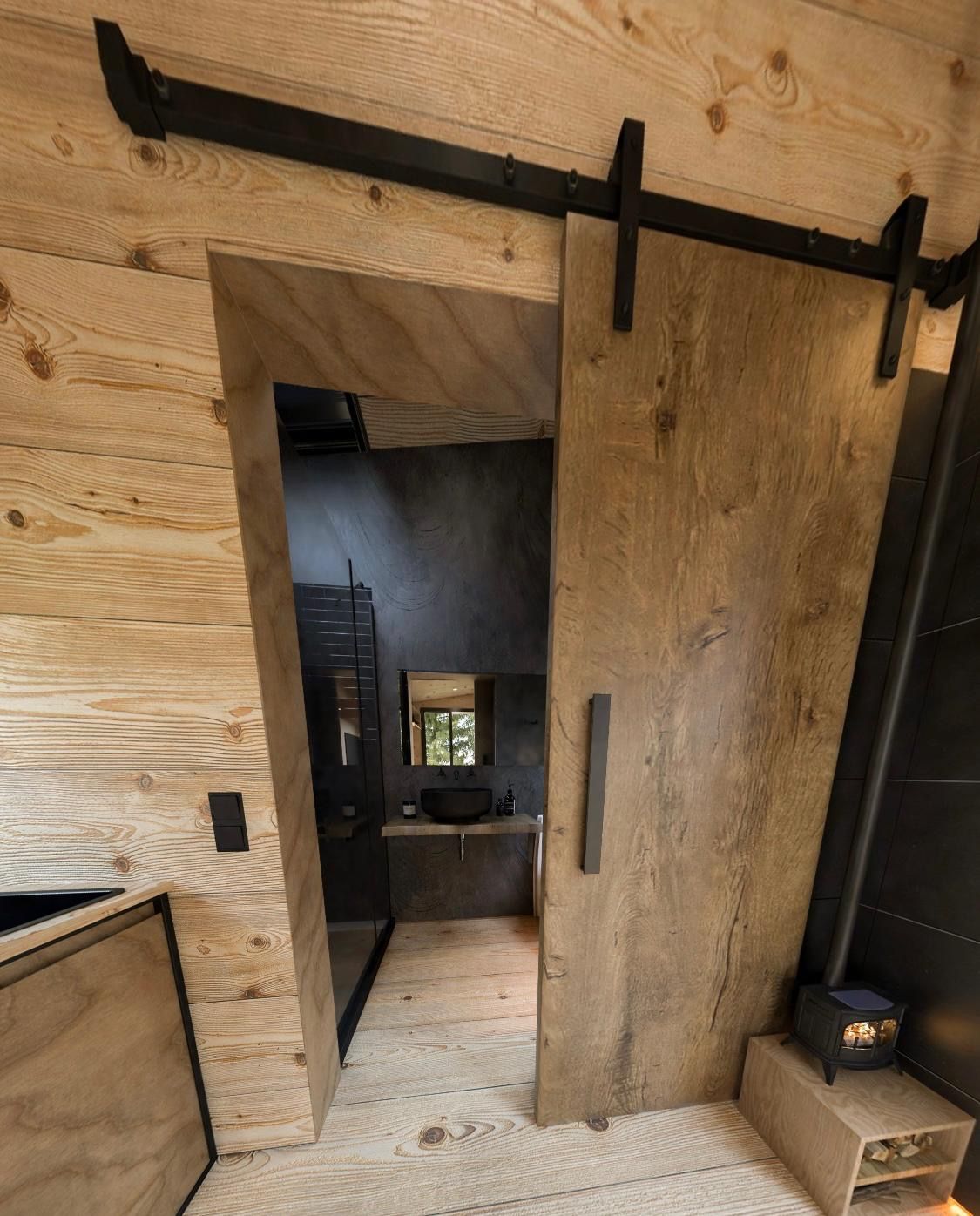 Wooden barn door on a track, revealing a small bathroom with a dark sink and mirror.