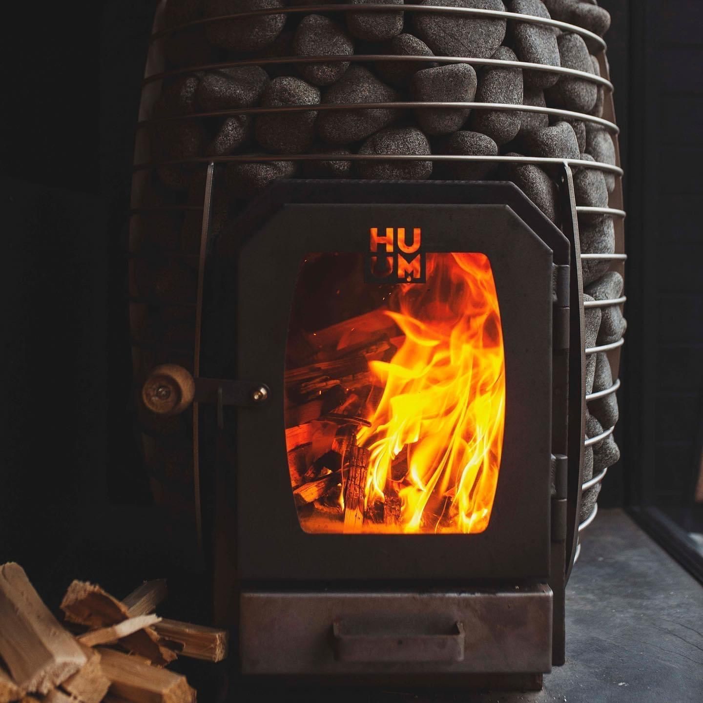 Wood-burning sauna heater with fire in the chamber. Stones are on top, wood logs at the base.