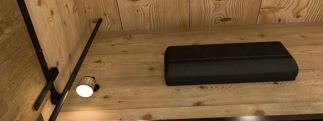 A dark, rectangular object sits on a wooden surface next to a light fixture and a black pole.