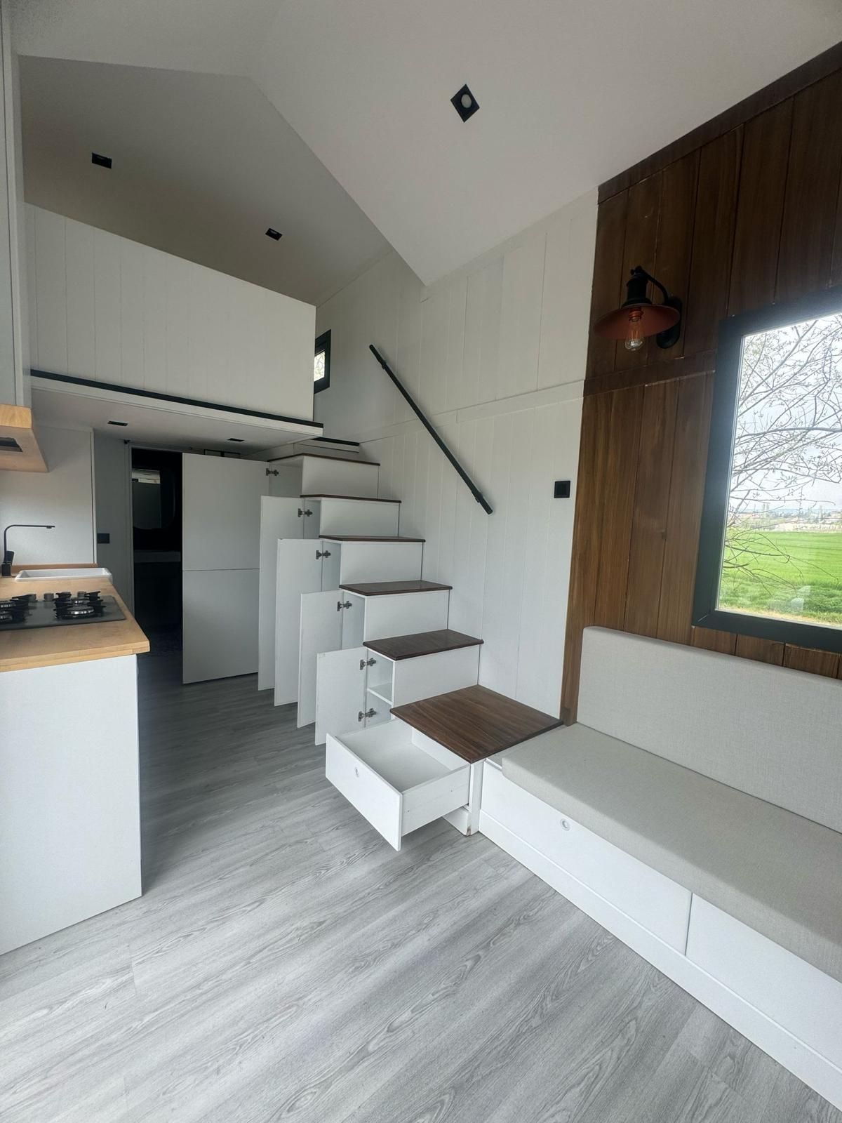 Tiny home interior with stairs containing storage drawers, a loft, and a seating area.