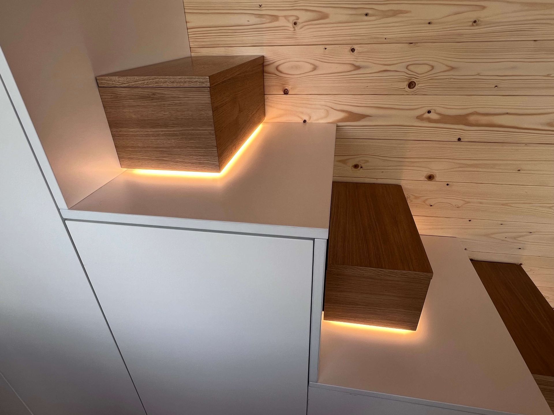 Staircase with white risers and wooden treads with warm LED lighting; wooden boxes on treads.