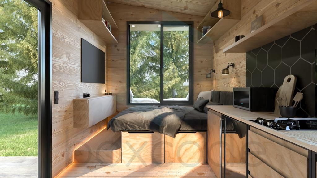 Cozy tiny home interior with bed, kitchen, and window looking out onto trees. Wooden walls and shelves.