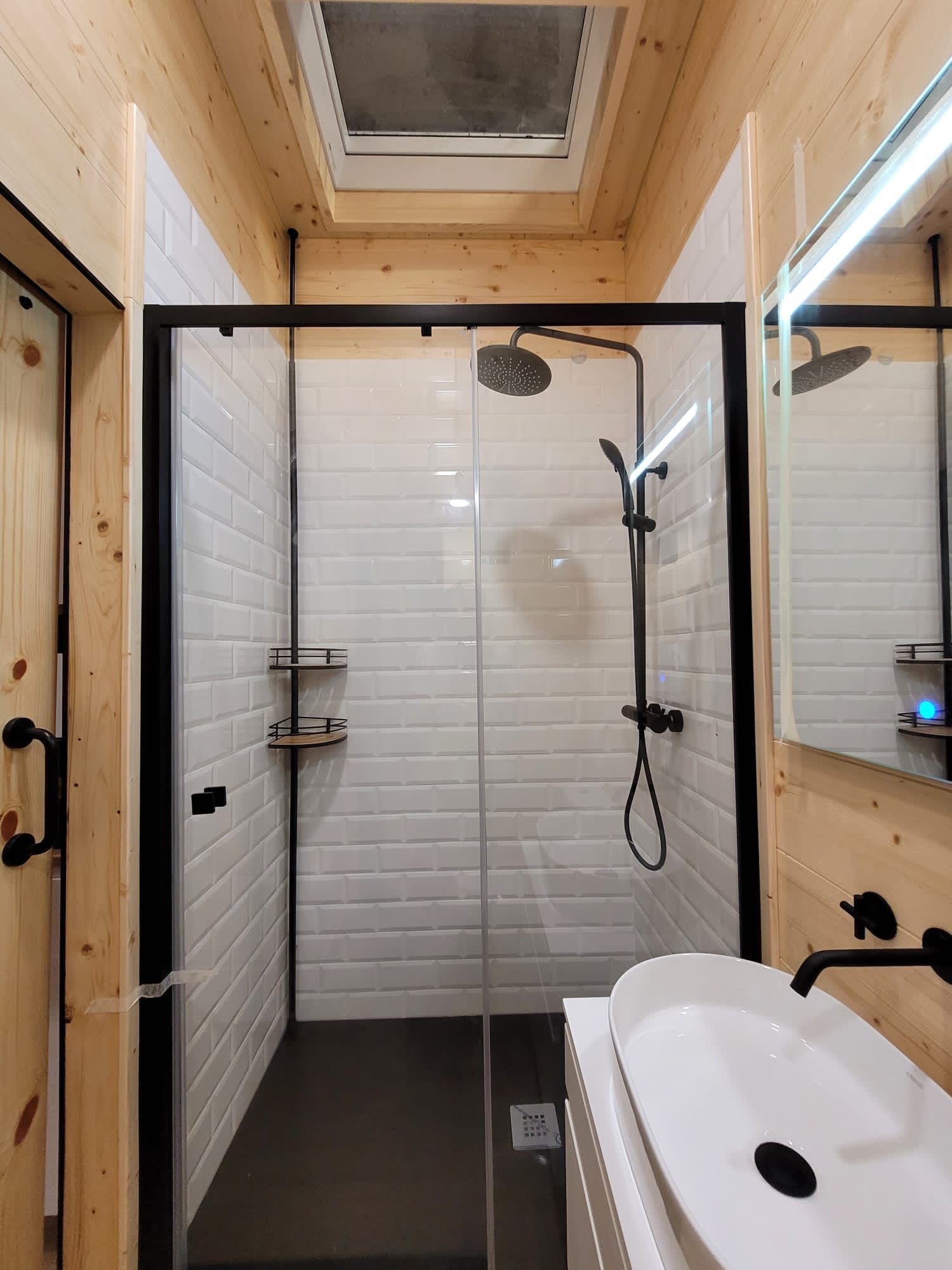Small bathroom with white subway tile, black shower frame and fixtures, wood accents.