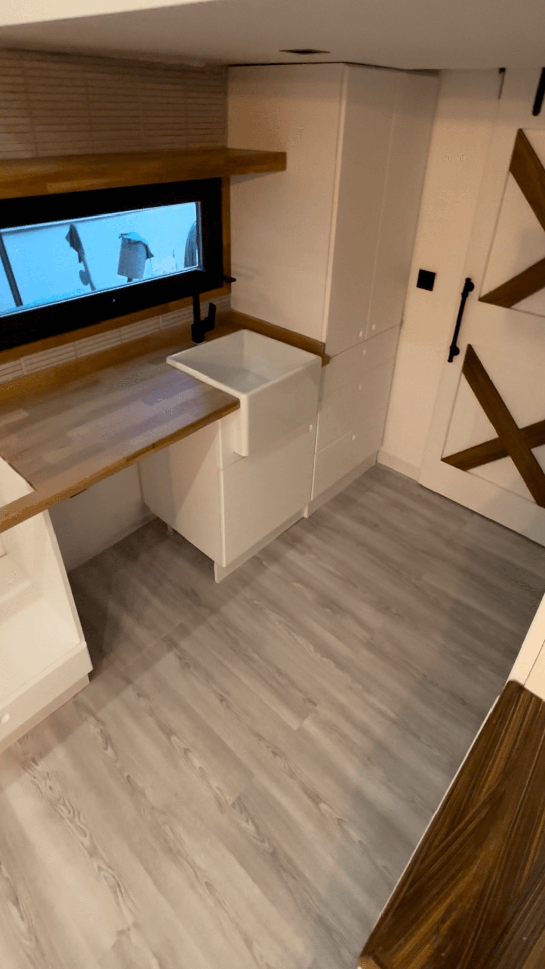 White built-ins with wooden accents, a small sink, and a barn door, in a room with wood-look flooring.