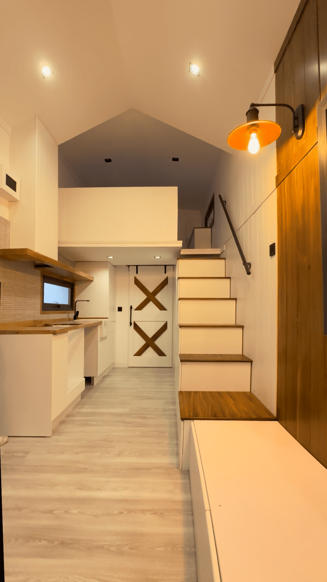 Tiny home interior with stairs to a loft, white and wood accents, overhead lighting.
