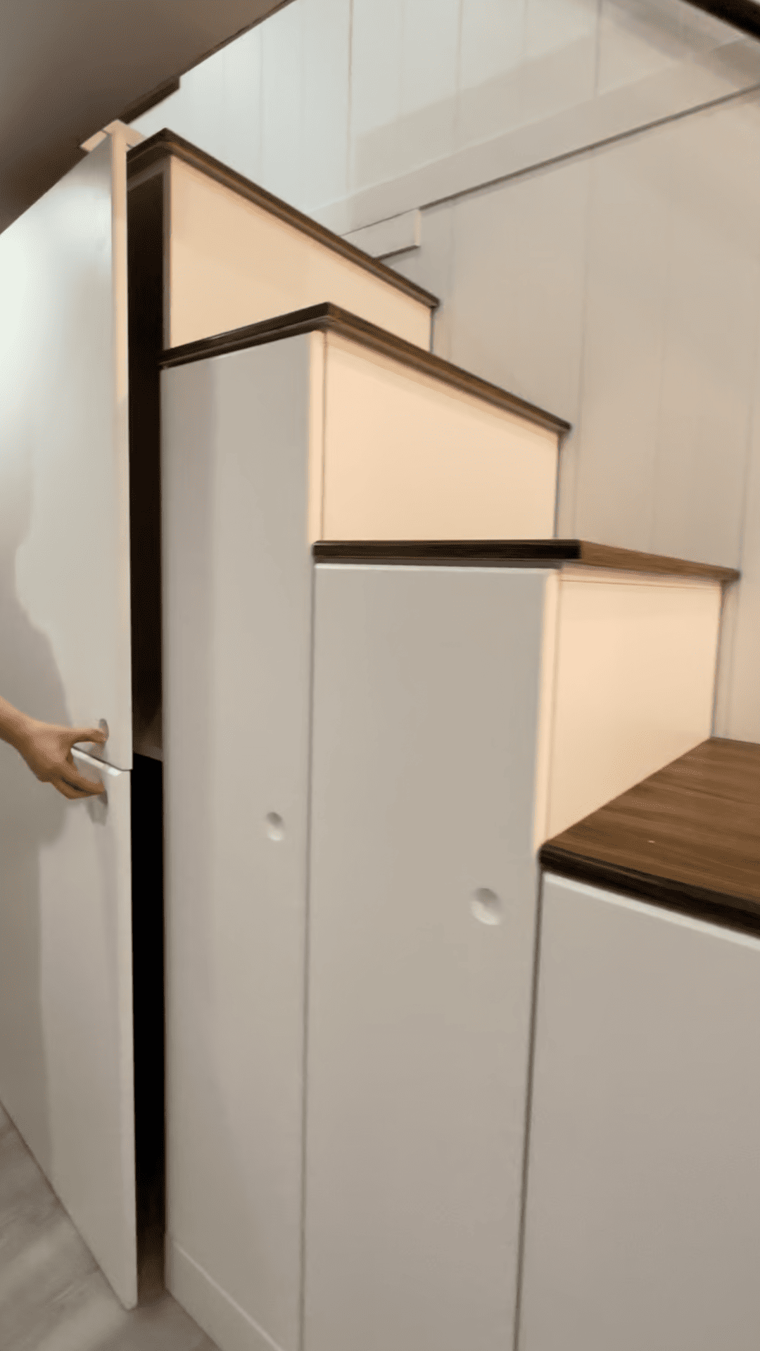 White storage stairs with a hand opening a hidden door. Dark wood steps.