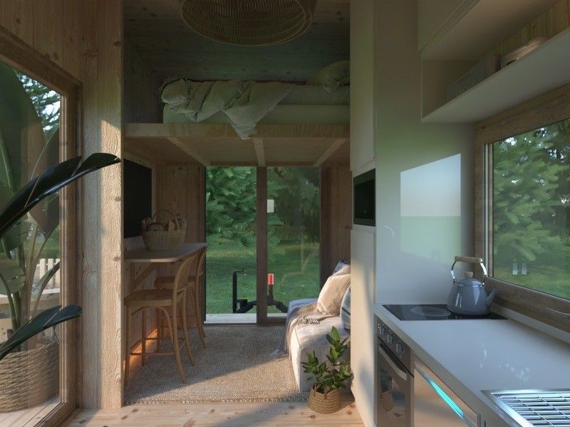 Cozy tiny house interior with a loft bed, kitchen, and large windows looking out onto a green landscape.