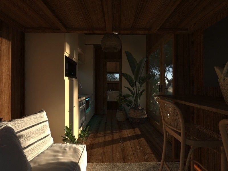Cozy cabin interior with wooden floors, sofa, kitchen, plants, and natural light streaming in.
