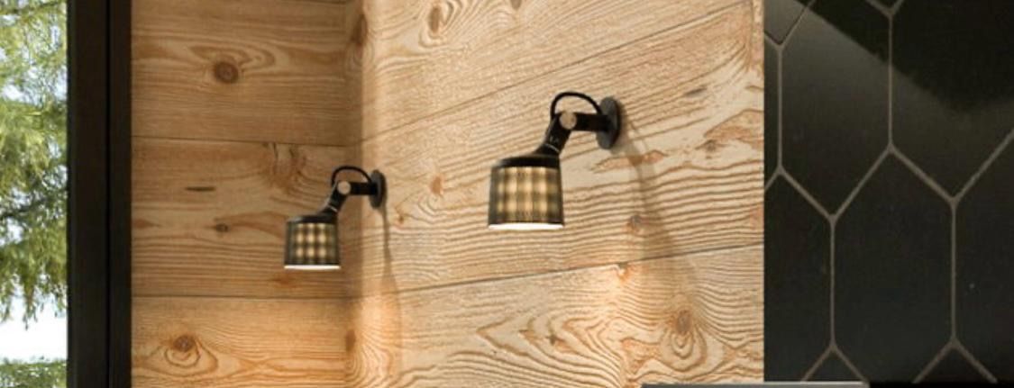 Two bronze sconces with plaid shades on a wood-paneled wall, next to dark hexagon tiles.