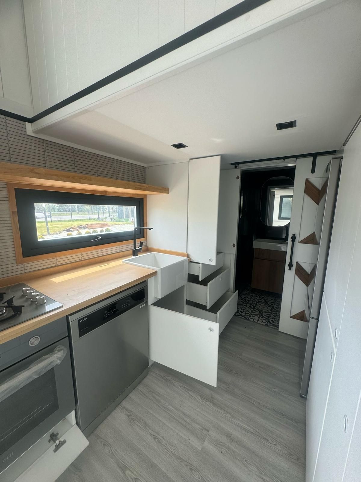 Tiny home kitchen with appliances, cabinets, wood countertops, and steps leading to bathroom.