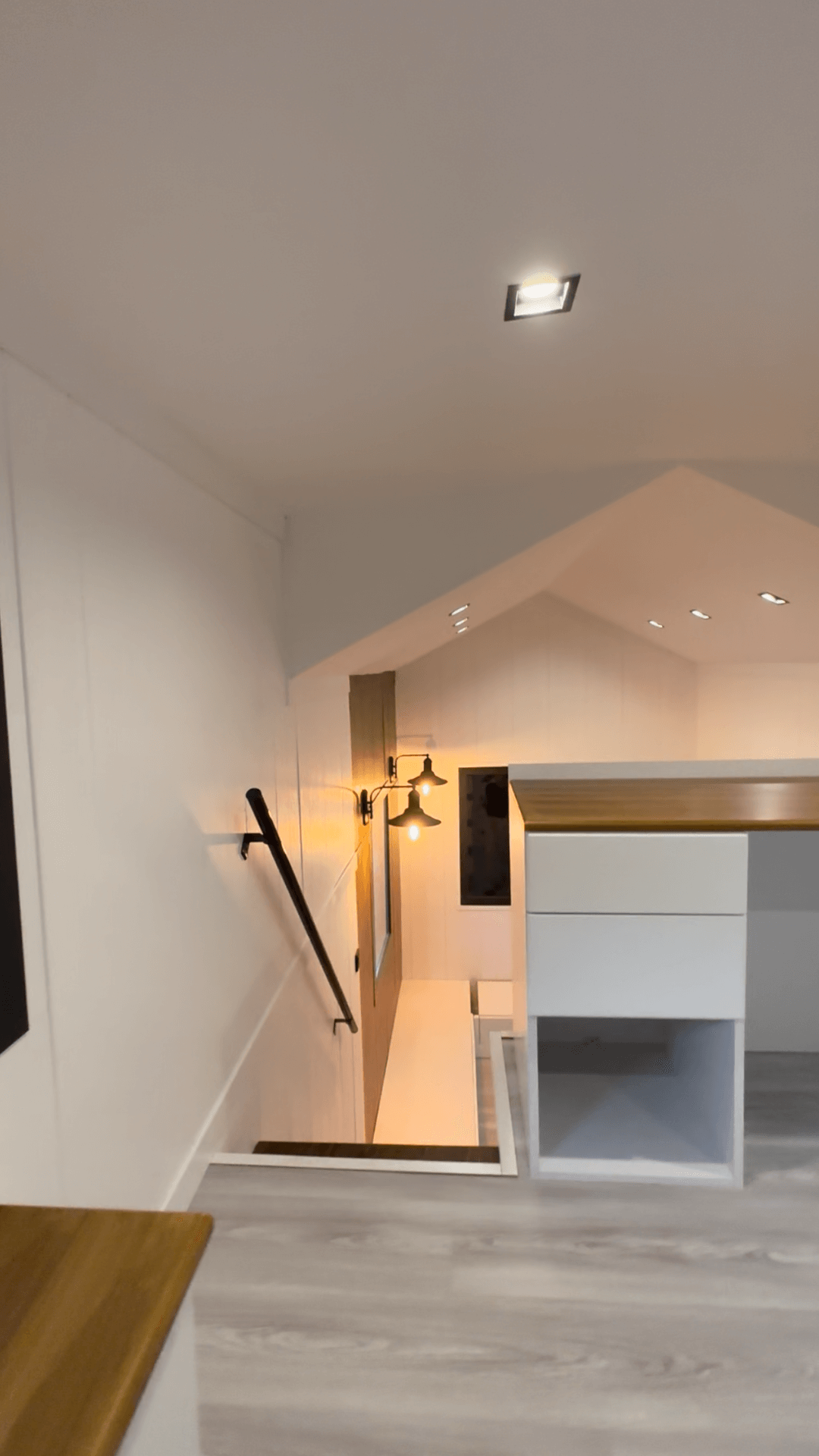 Staircase descending, black railing, light wood accents, white walls, overhead lights, contemporary design.