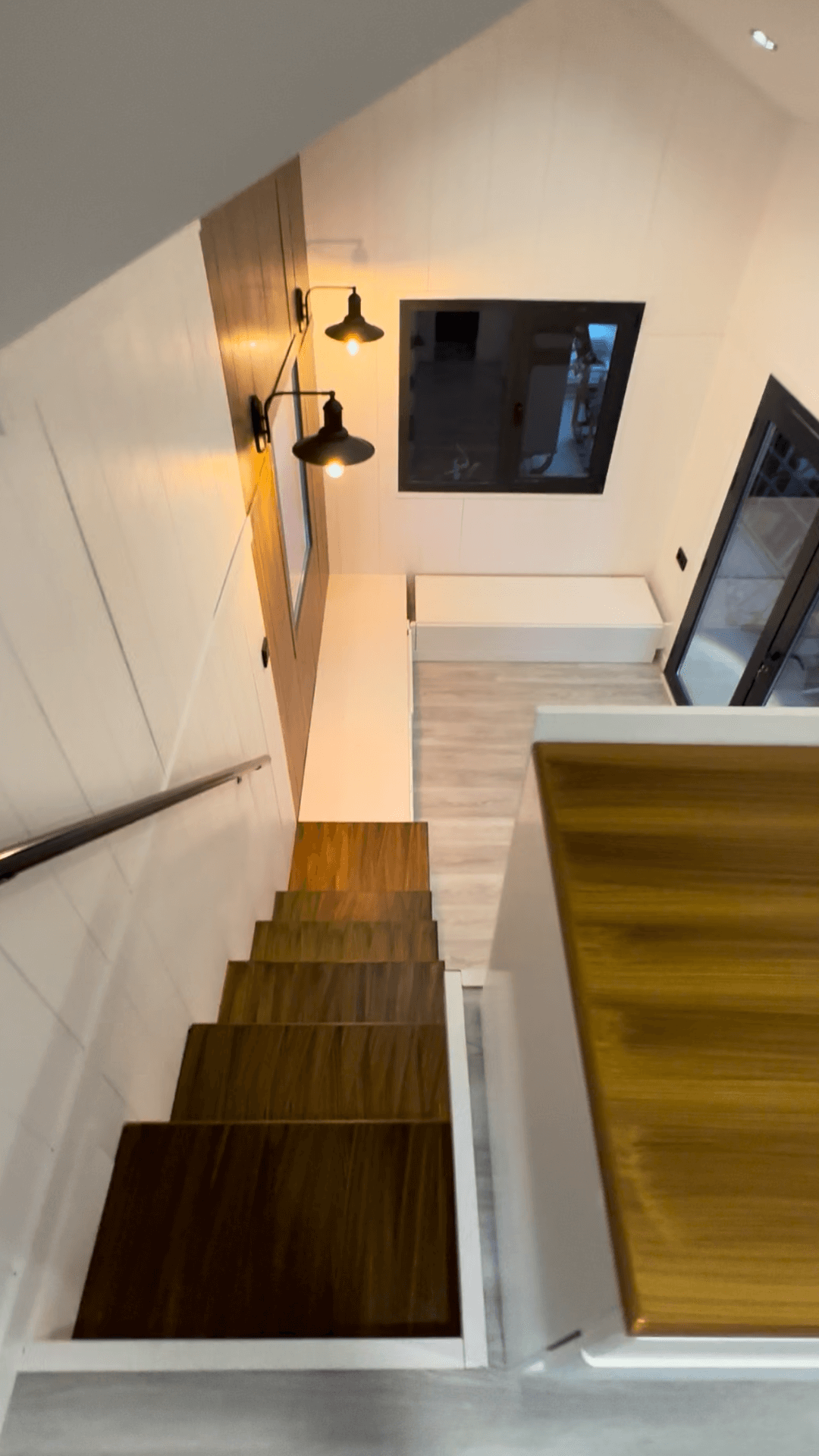 Staircase with wooden steps, white walls, and black sconce lights. Descending view.