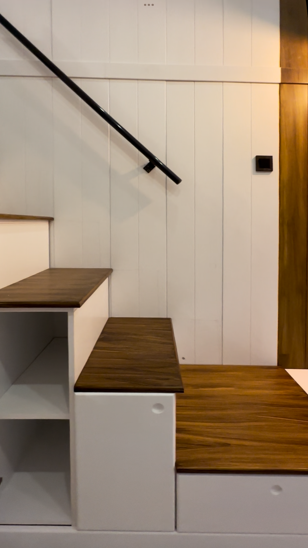 White stairs with wood treads and black handrail in a tiny home.
