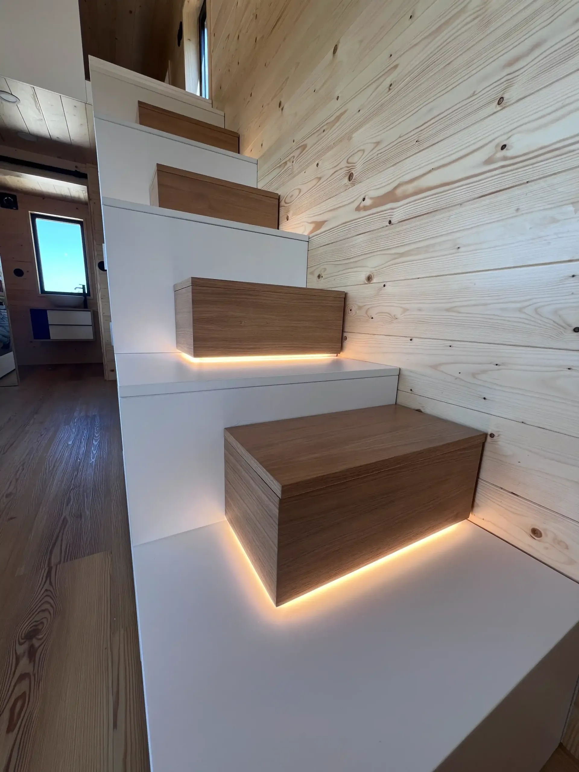 Wooden staircase with built-in boxes and under-step lighting in a light wood interior.