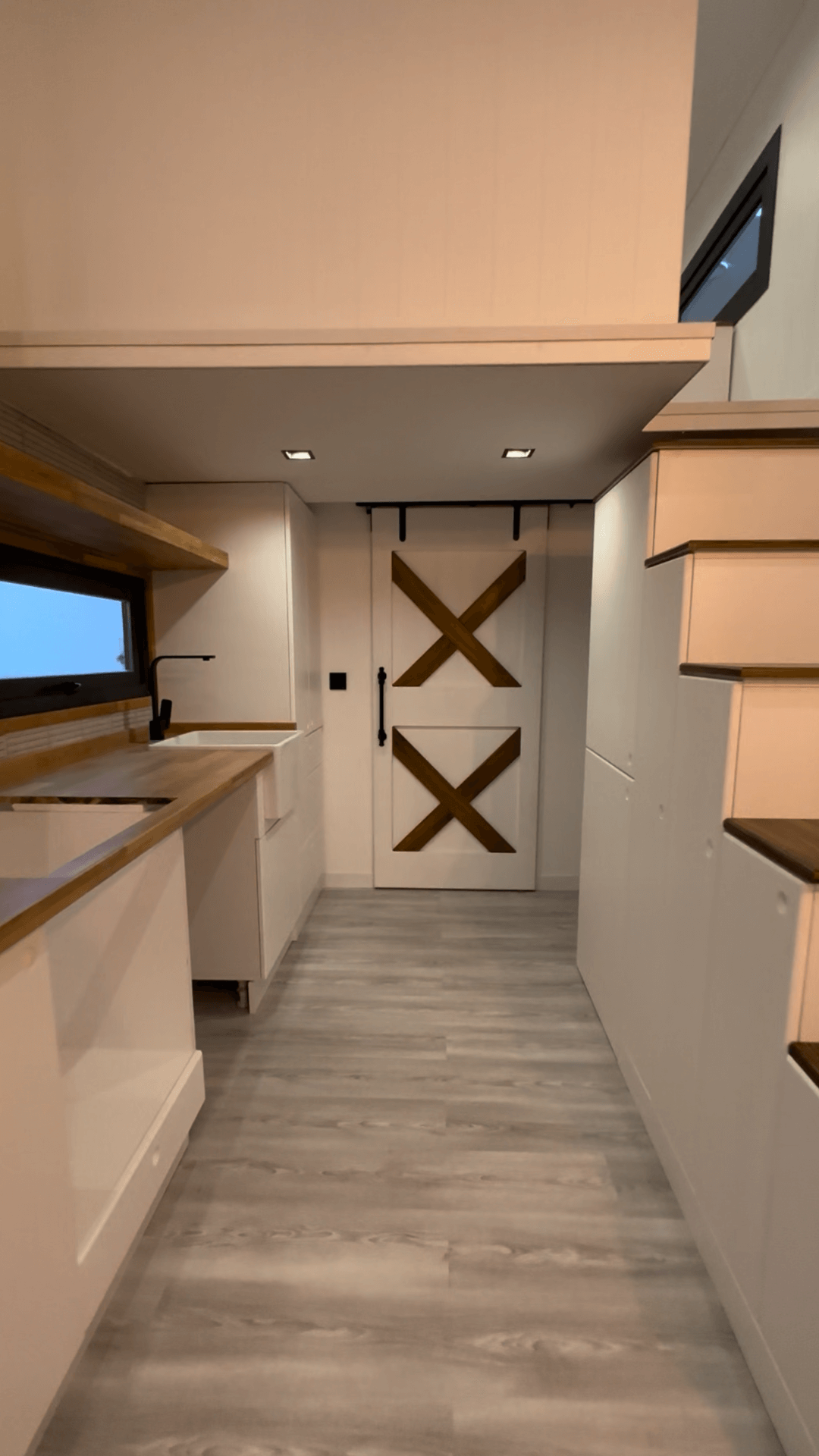 Narrow interior hallway with a white and wood barn door, kitchen, and stairs to a loft.