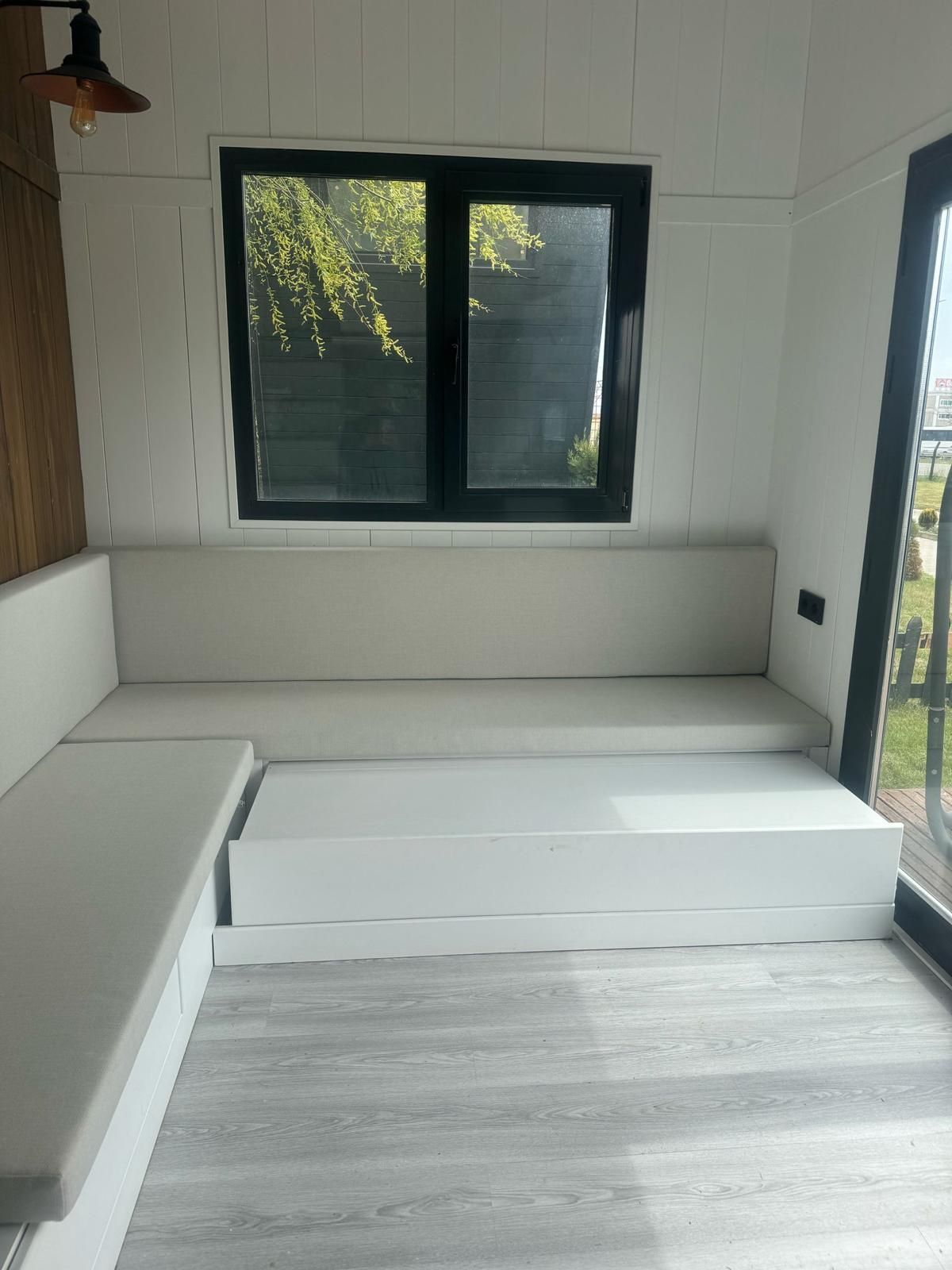 White interior with a built-in sofa, small window, and wood-paneled wall.