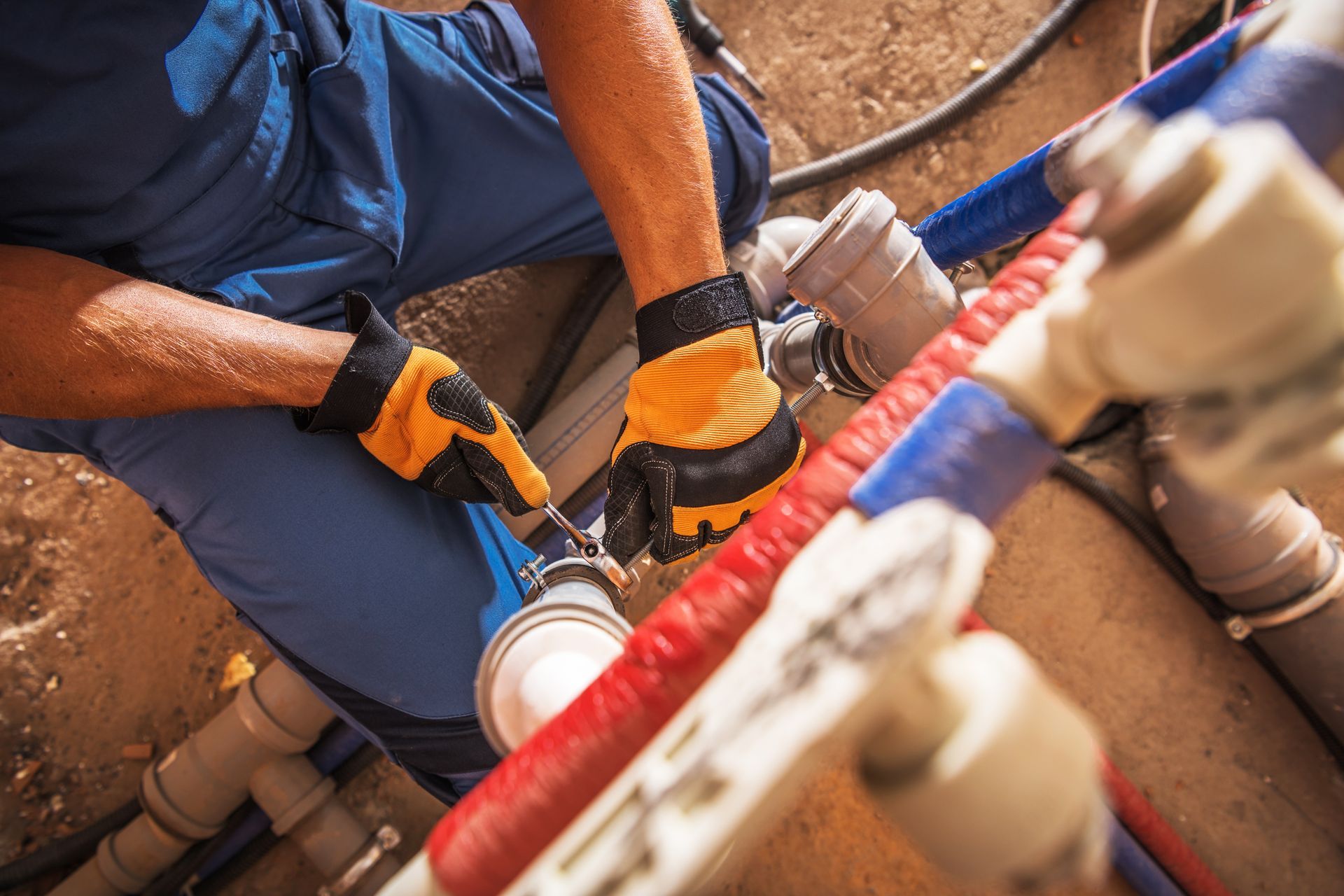 Plumber in blue workwear connecting pipes with a wrench, wearing gloves.