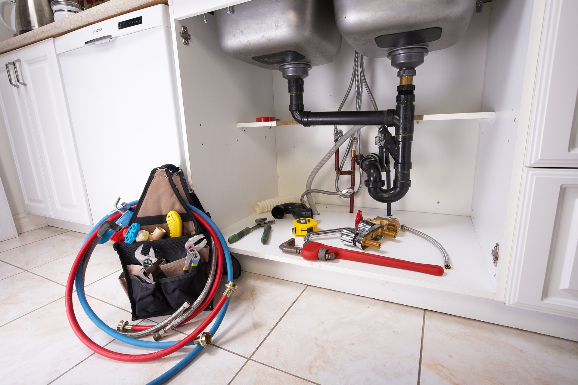 Plumbing tools and supplies under a kitchen sink, including hoses and a toolbox.