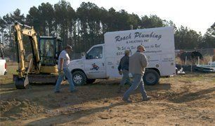 Men near Roach Plumbing truck and excavator at a construction site.