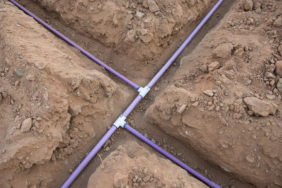 Purple PVC pipes in trenches, connected with white fittings, in brown soil.