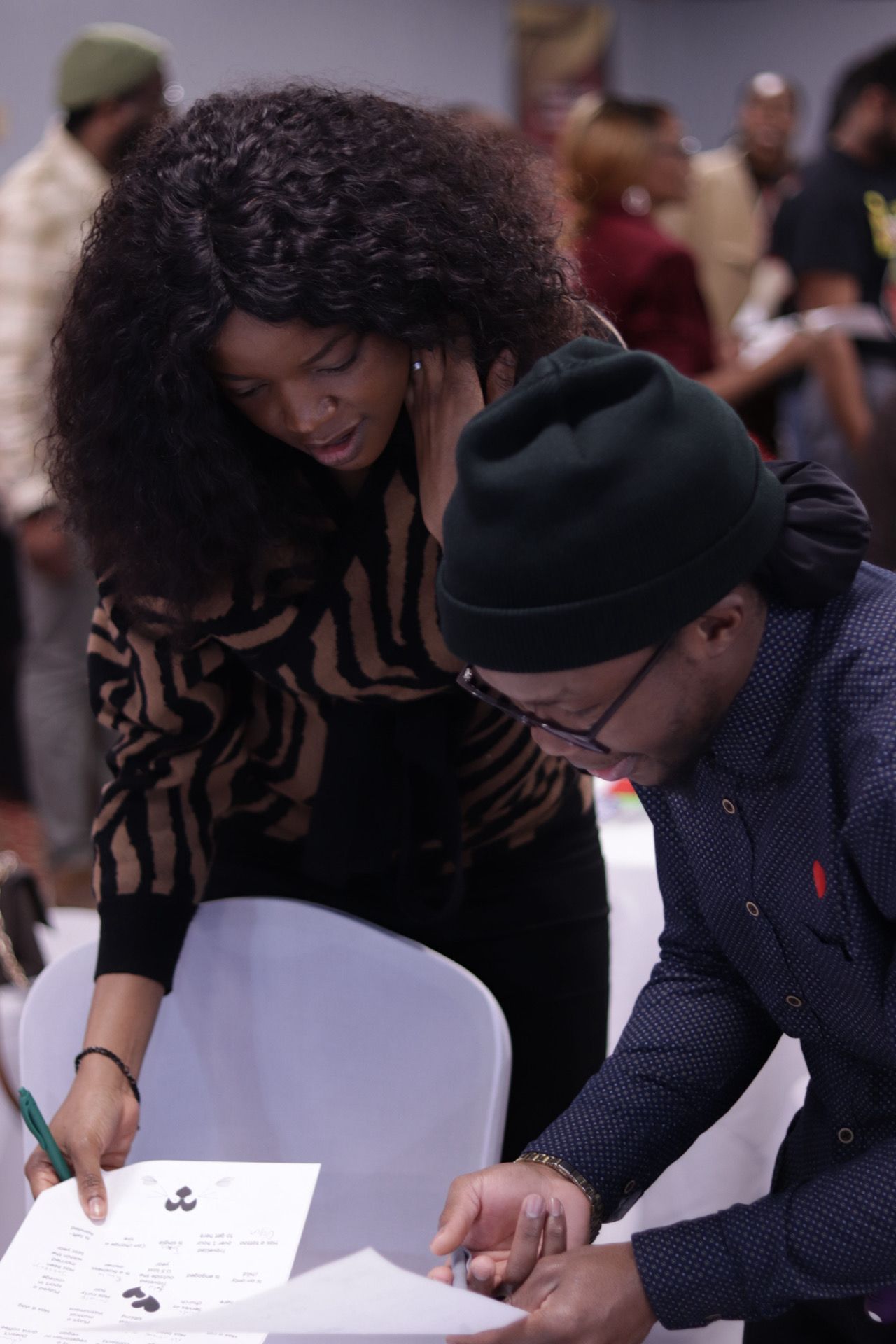 Woman with curly hair and man in a beanie looking at papers at a table indoors.