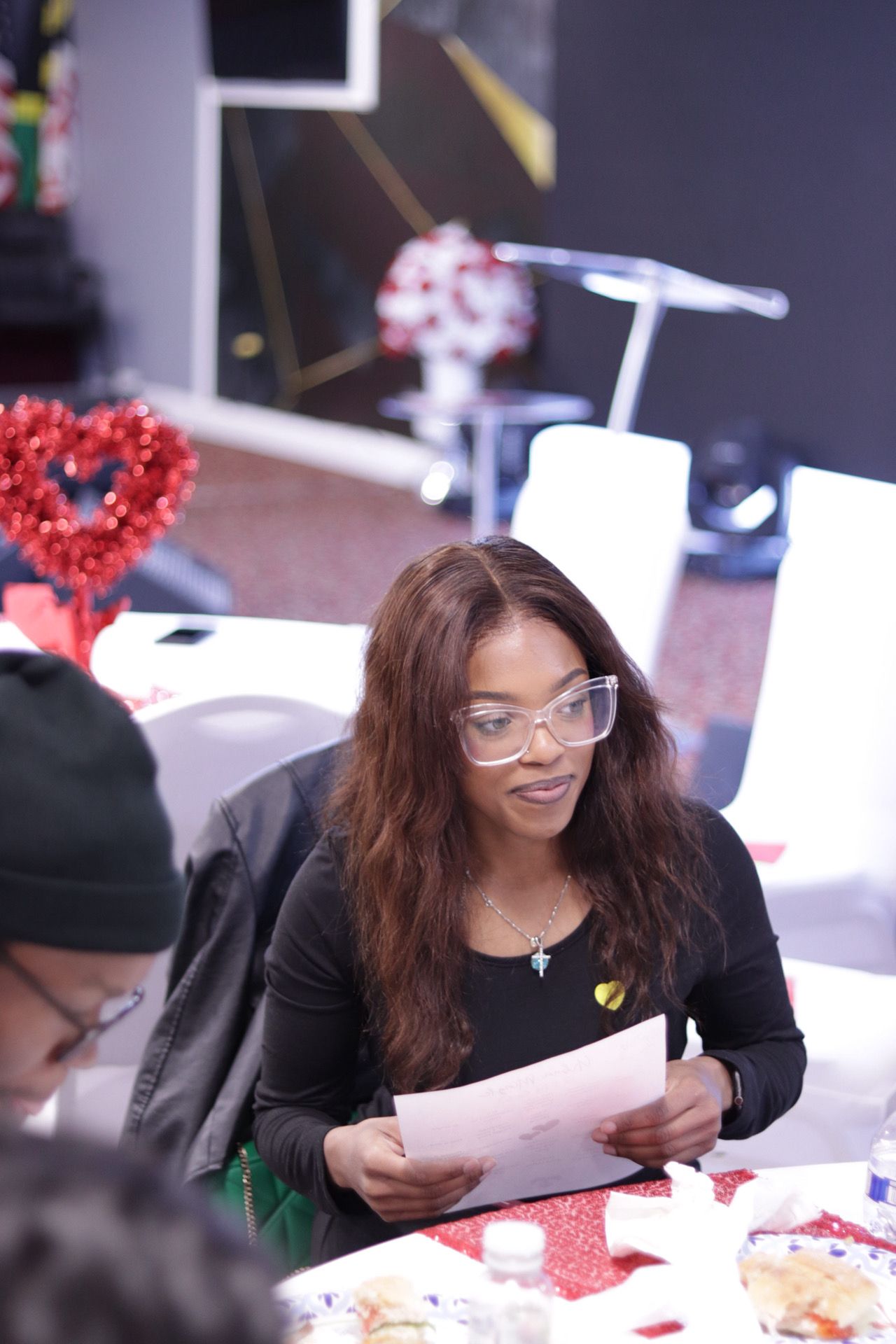 Woman with glasses reads a paper at a table decorated with red hearts.