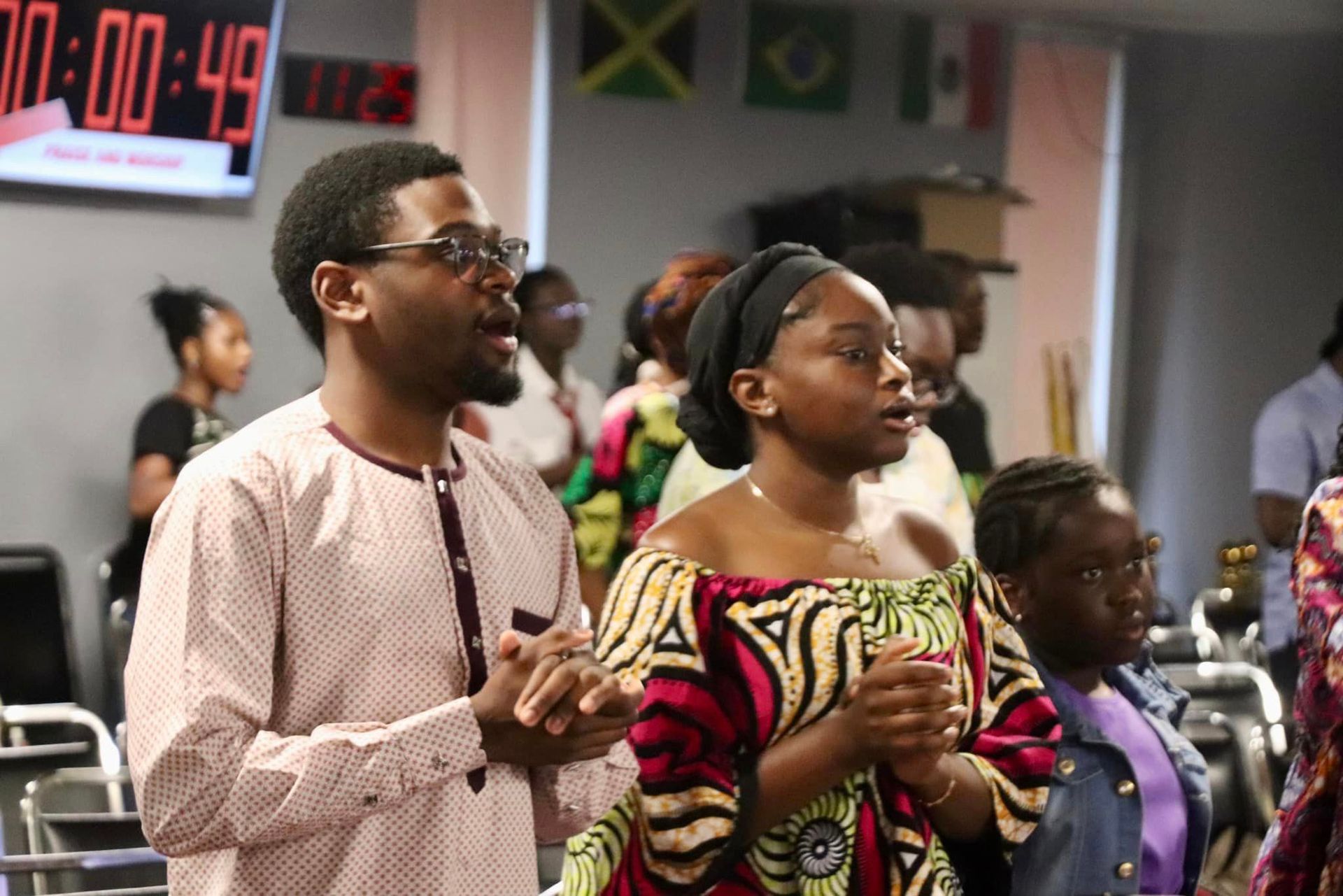 People of color in a church, singing, praying with hands raised.