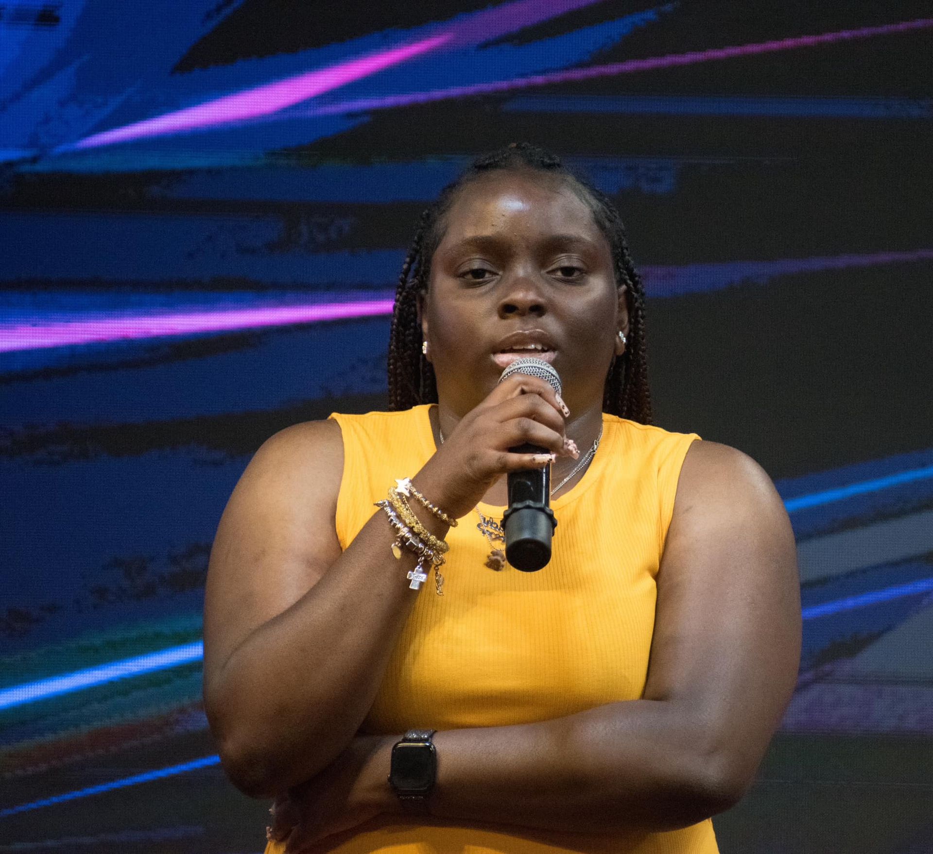 Woman in yellow dress speaking into microphone on stage.