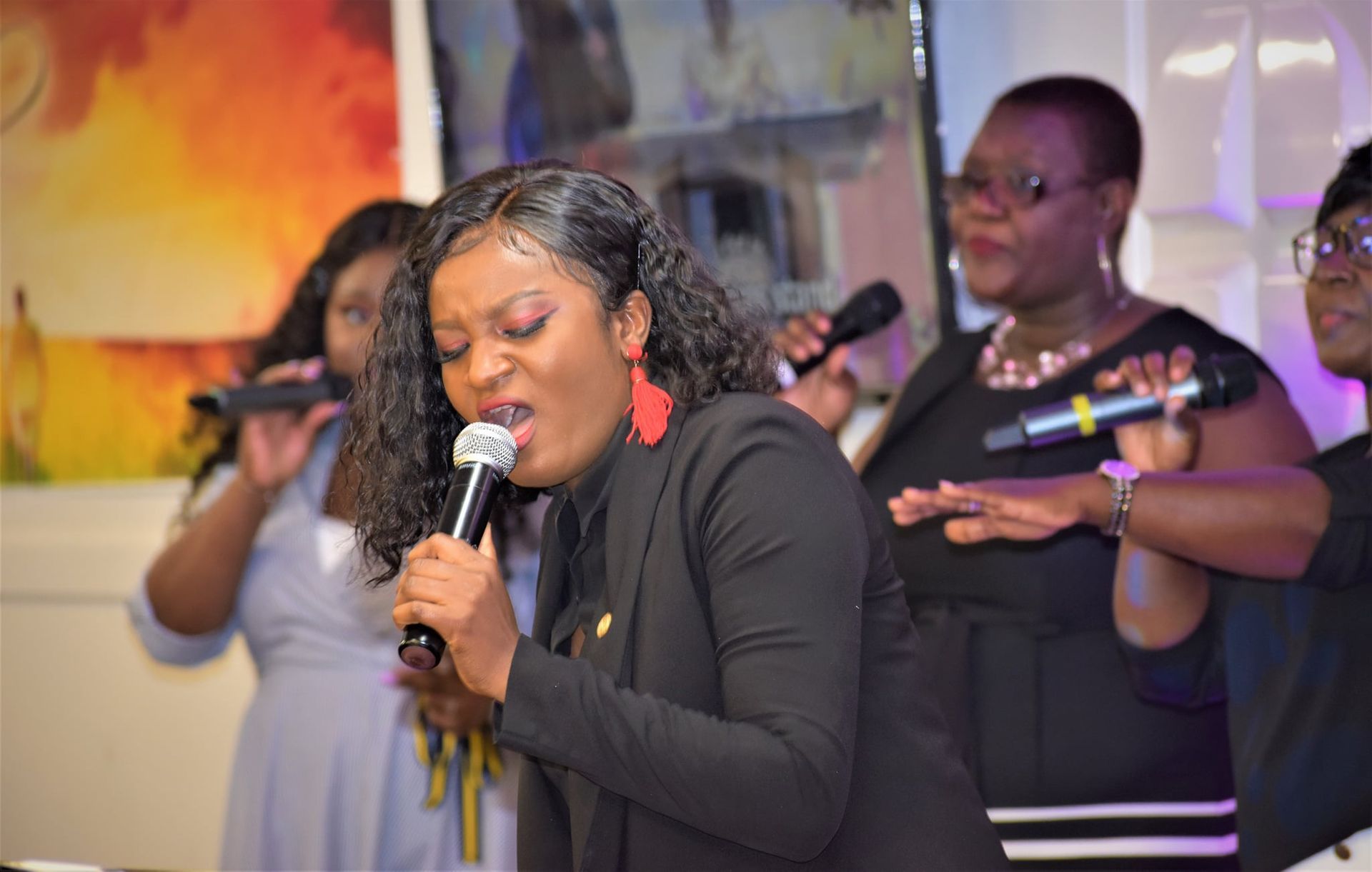 Choir of Black women singing with microphones in a brightly lit setting.