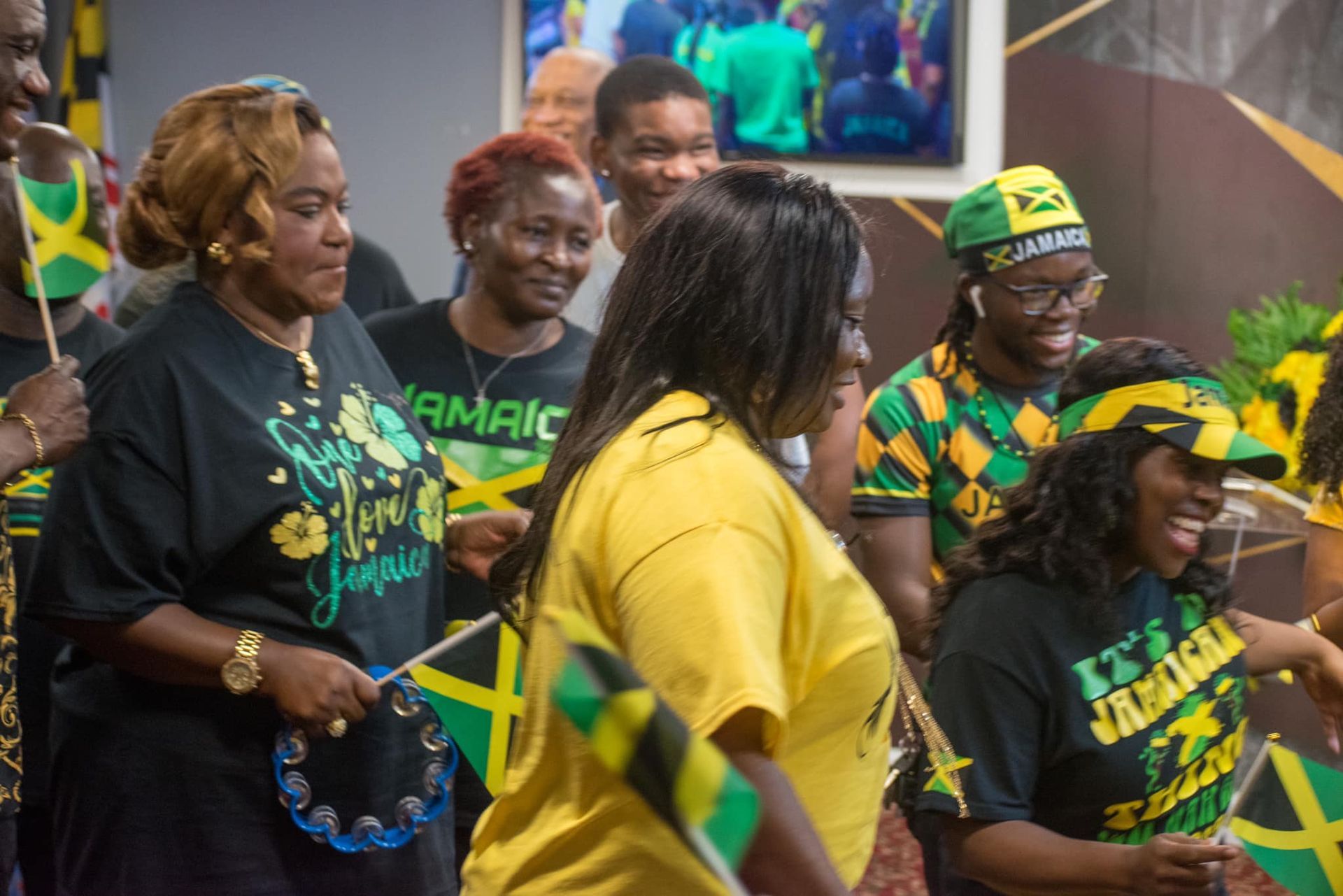 People celebrating, some holding Jamaican flags, wearing yellow and green clothing, smiling.