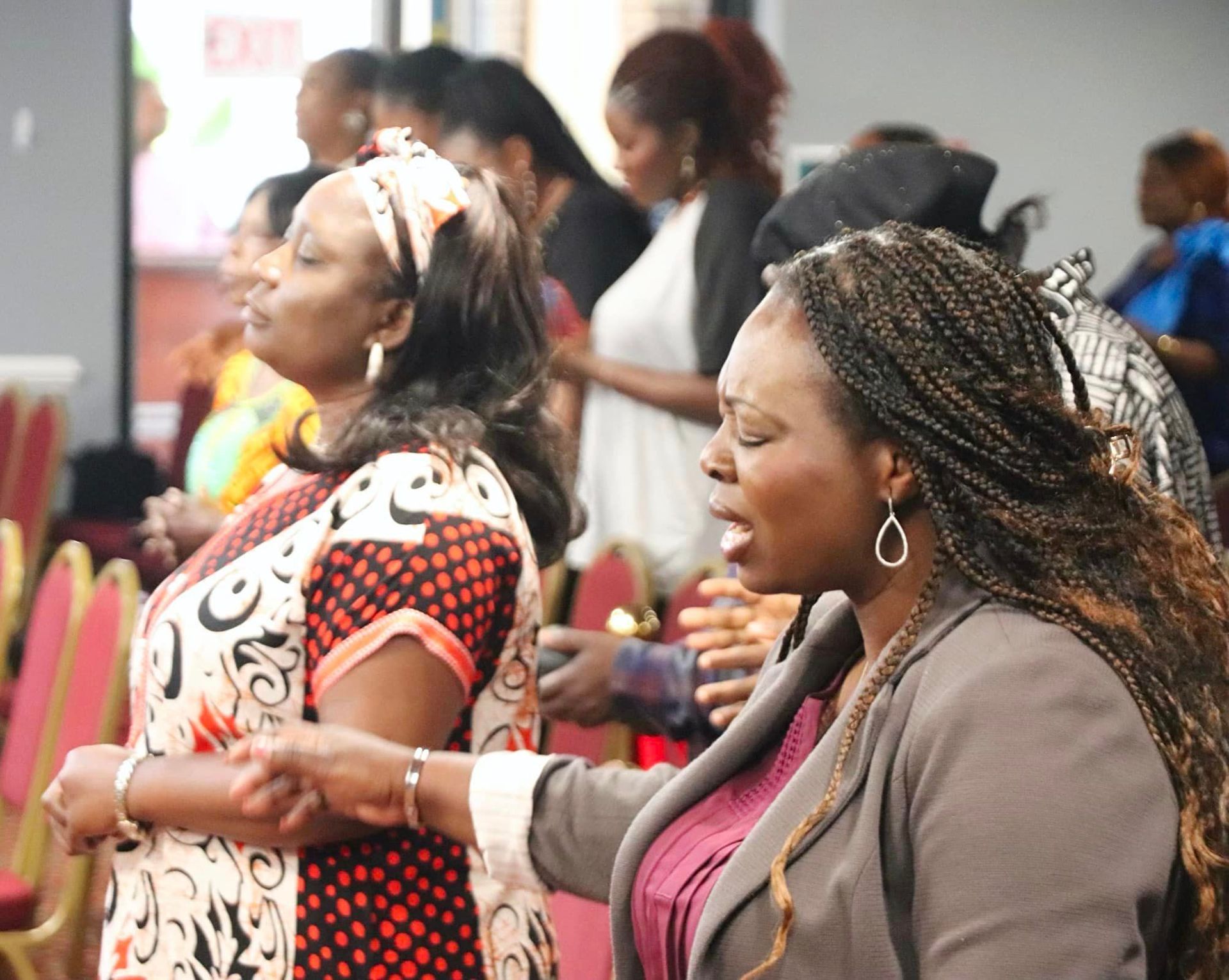 Group of women in a church service, eyes closed in prayer, some with hands raised.
