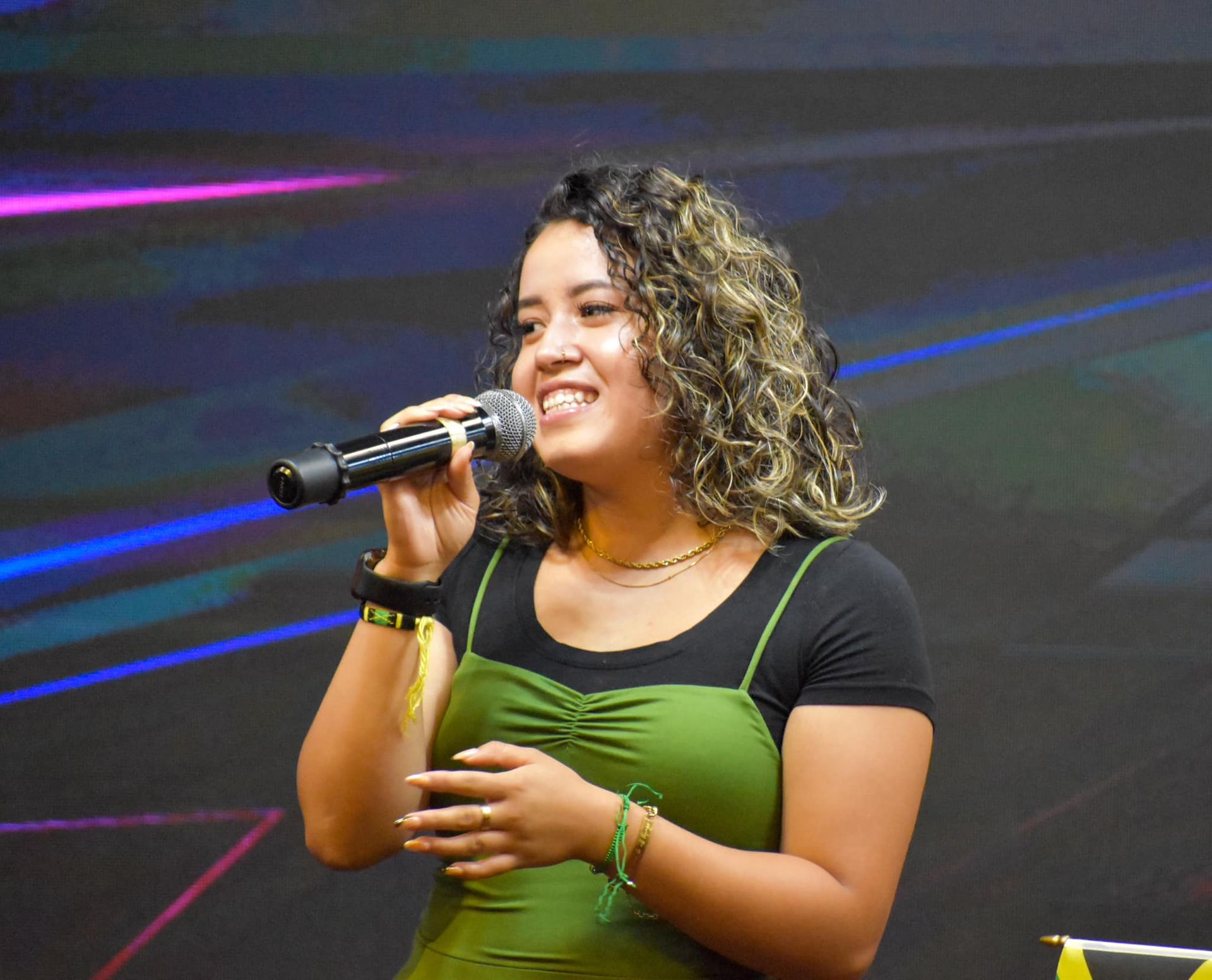 Woman with curly hair singing into a microphone; wearing a green dress.